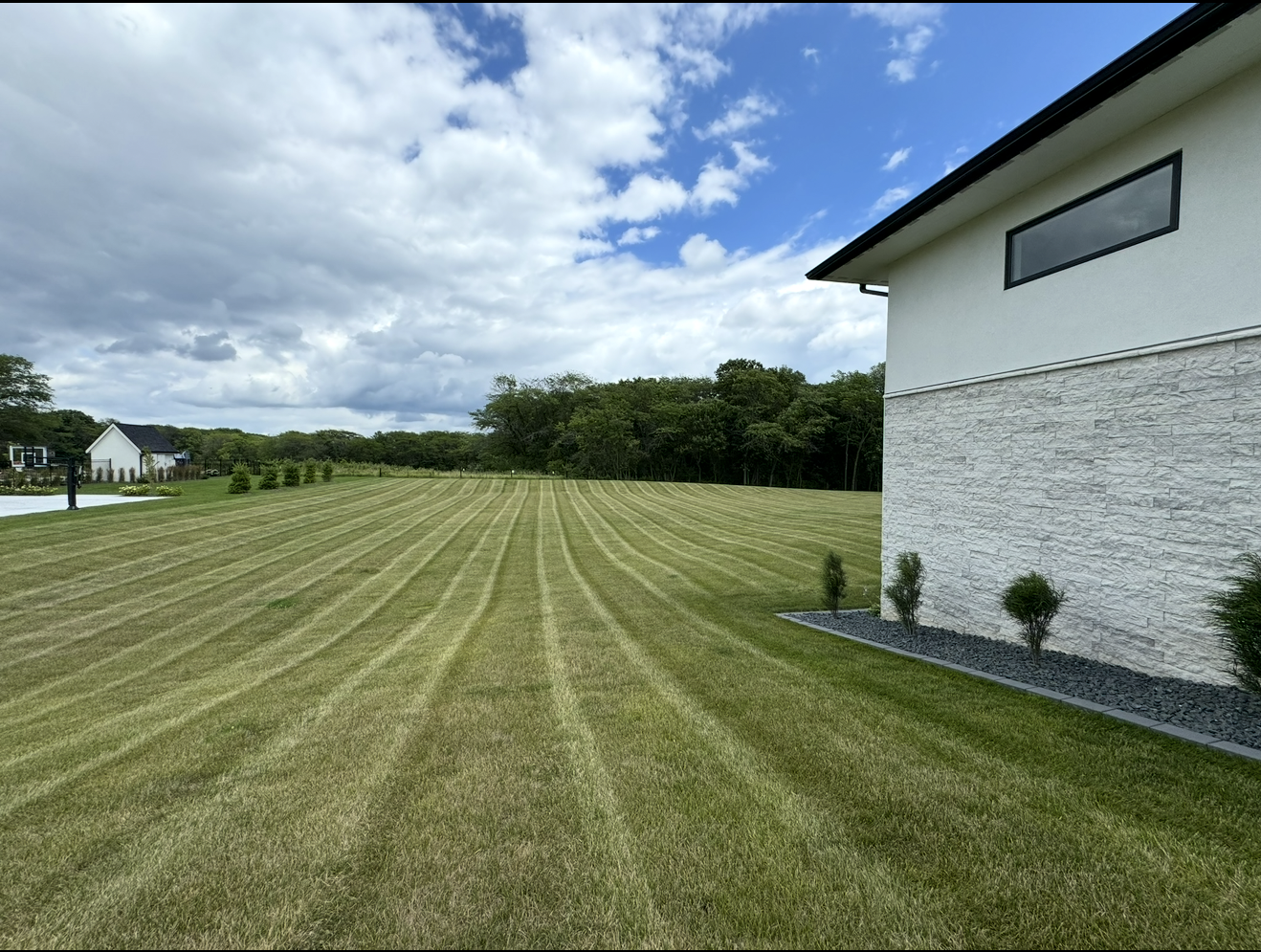Wide mowed lawn beside a white house under a blue sky with clouds