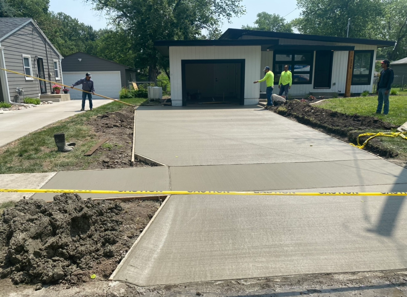 Concrete driveway leading to a modern house garage, with workers and yellow caution tape in front.