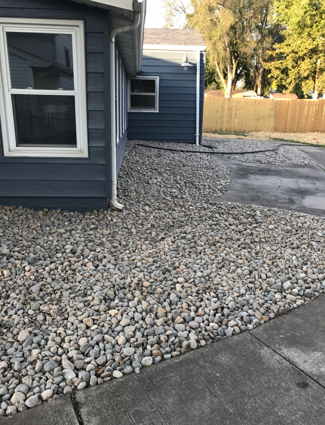 Blue house exterior with gravel yard and concrete driveway along the side of the home