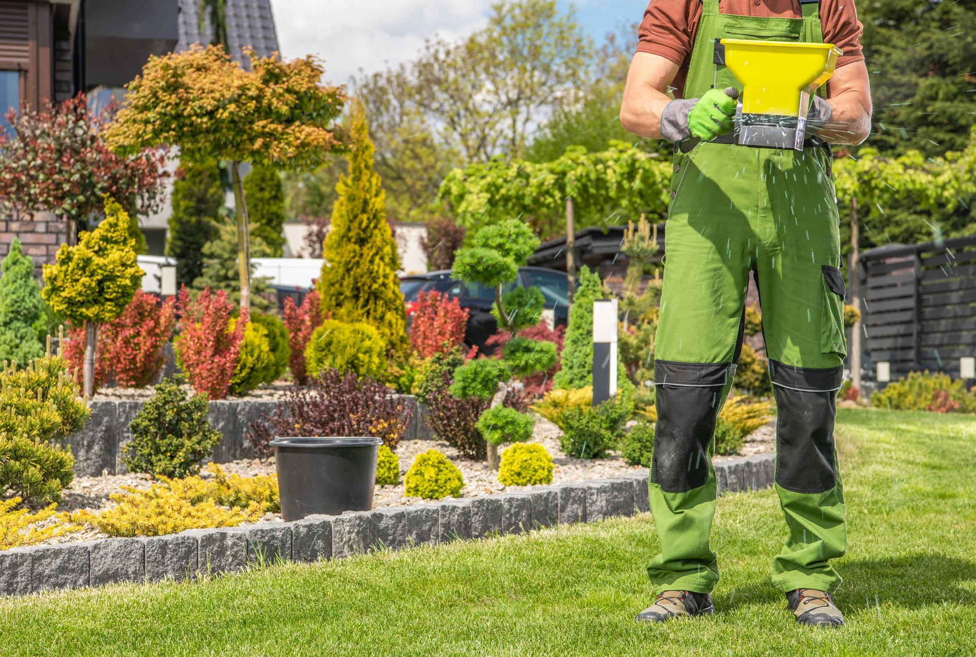 Person holding a yellow spreader in a colorful garden landscape with manicured shrubs and flowers