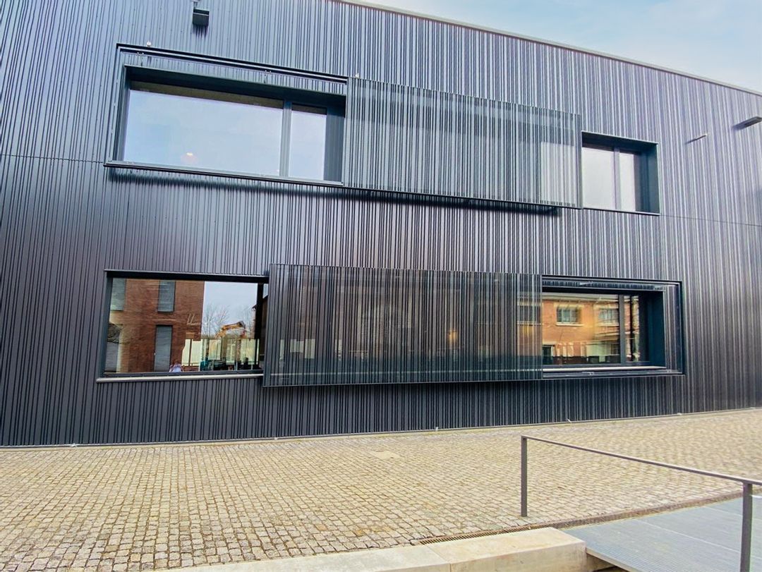 Modern building with dark, textured facade and rectangular windows.