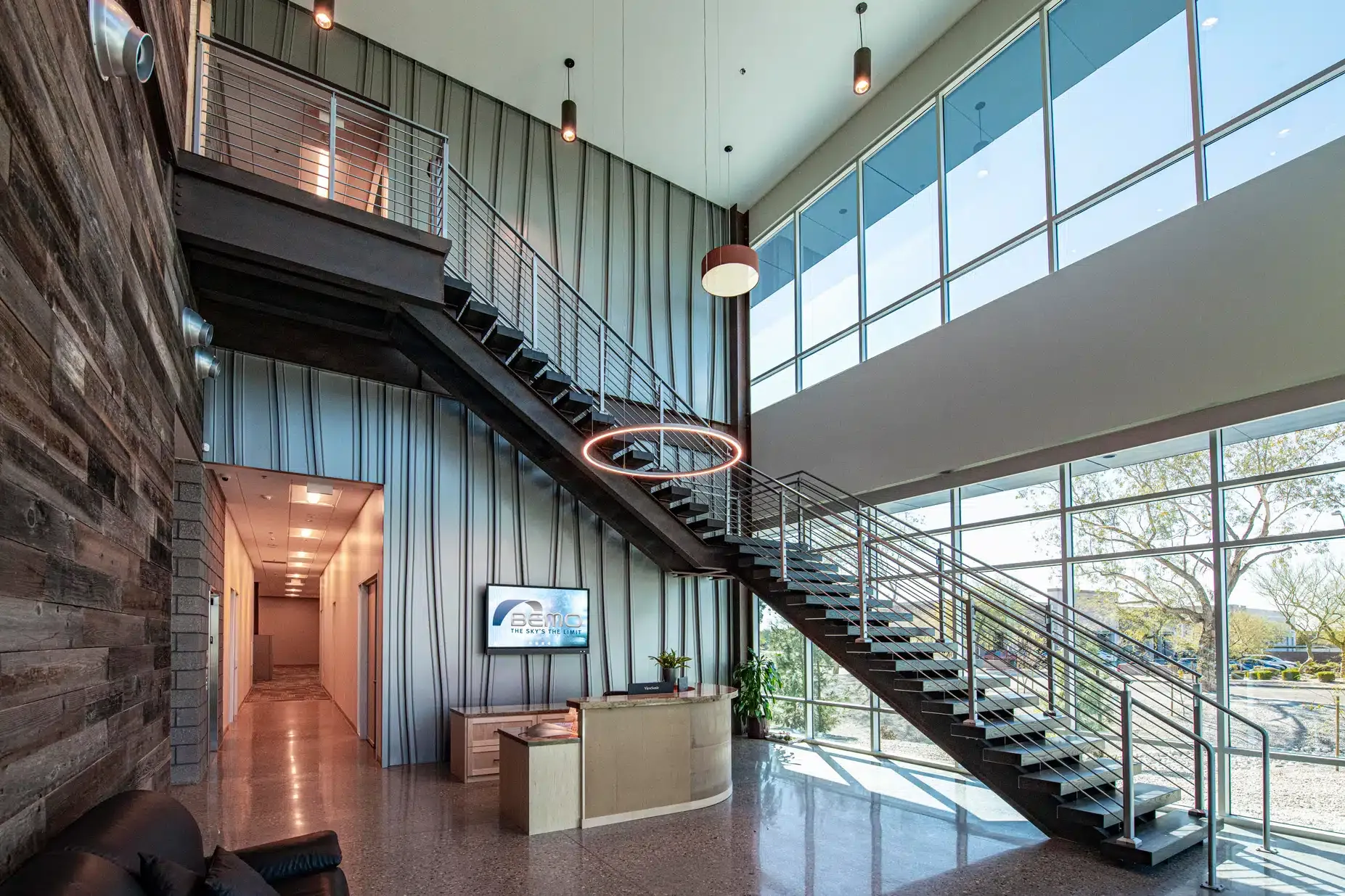 Modern office lobby with staircase, large windows, and stone accent wall.