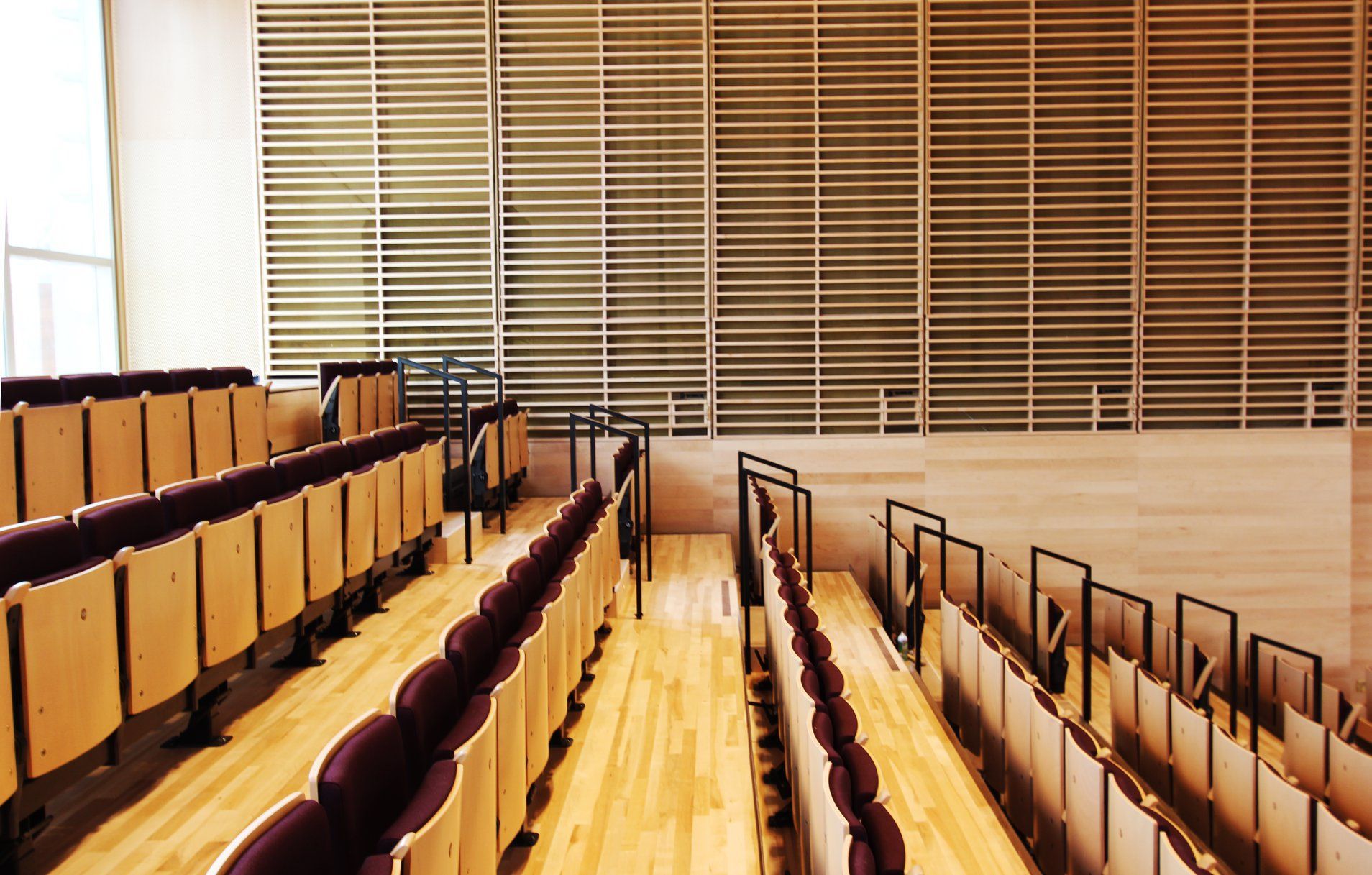 Rows of empty wooden theater seats facing a wall of horizontal wooden slats.