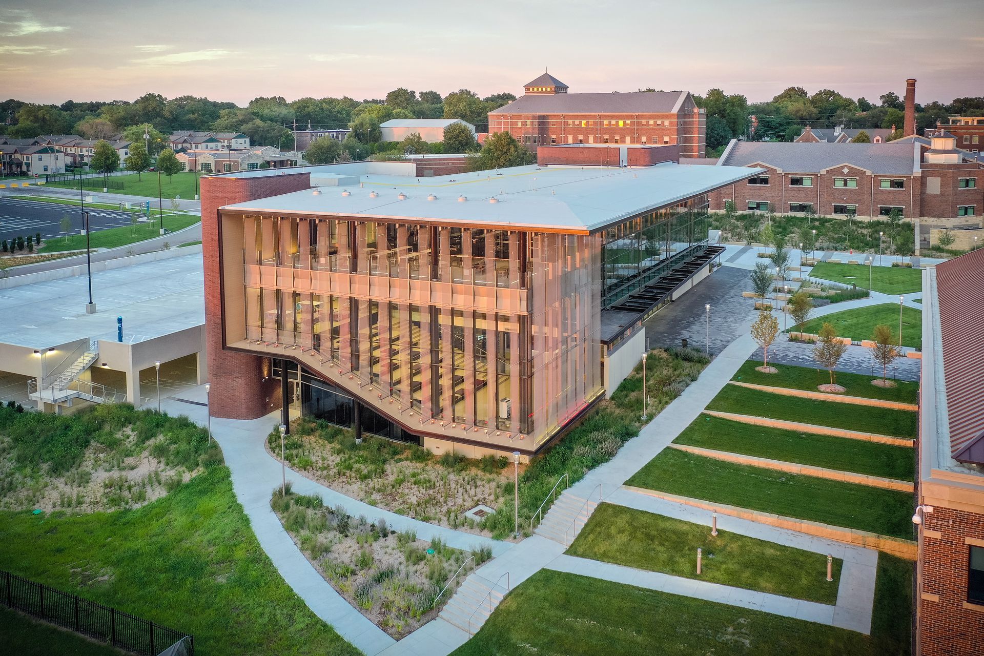 Modern university building with wooden exterior and glass panels, green lawn, and other brick buildings.