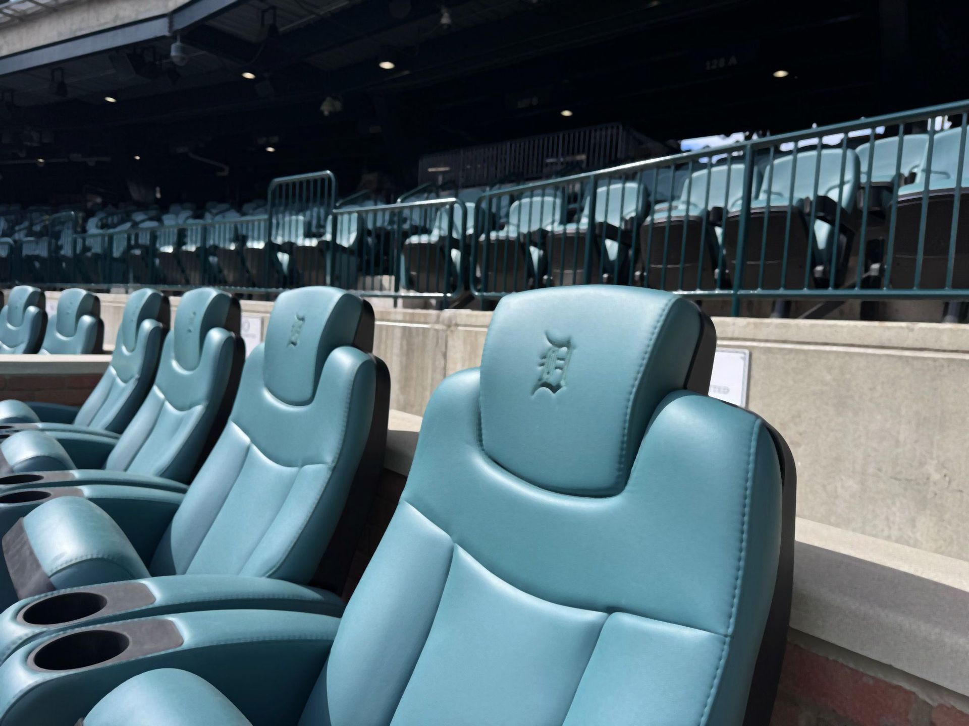 Row of teal leather seats with cup holders in a stadium, likely for premium viewing.