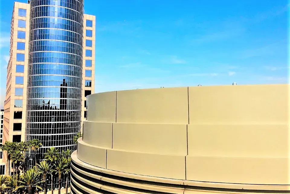 A tall glass building next to a multi-tiered tan circular building under a clear blue sky.