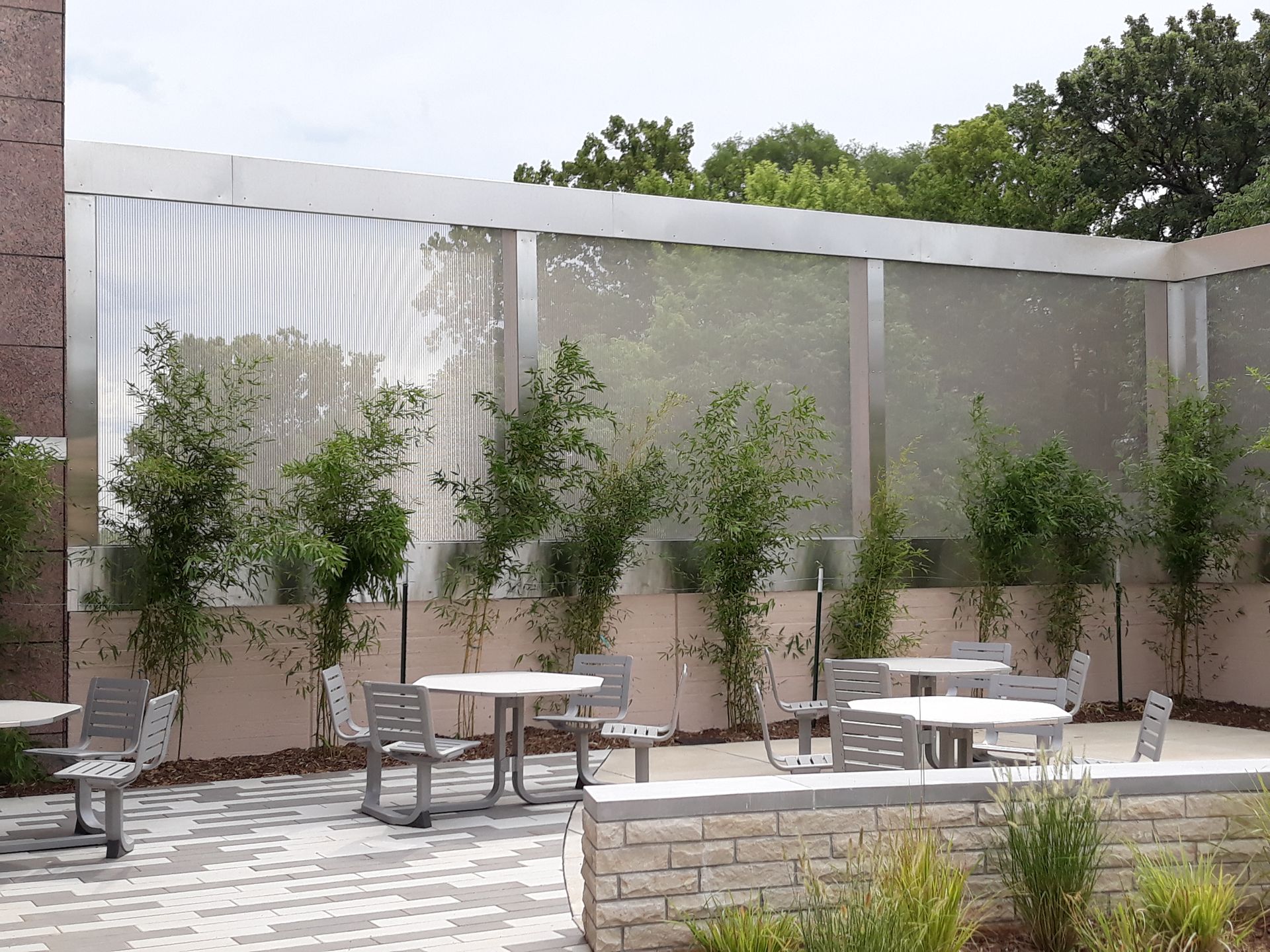 Outdoor patio with tables, chairs, and trees, enclosed by a perforated metal wall.