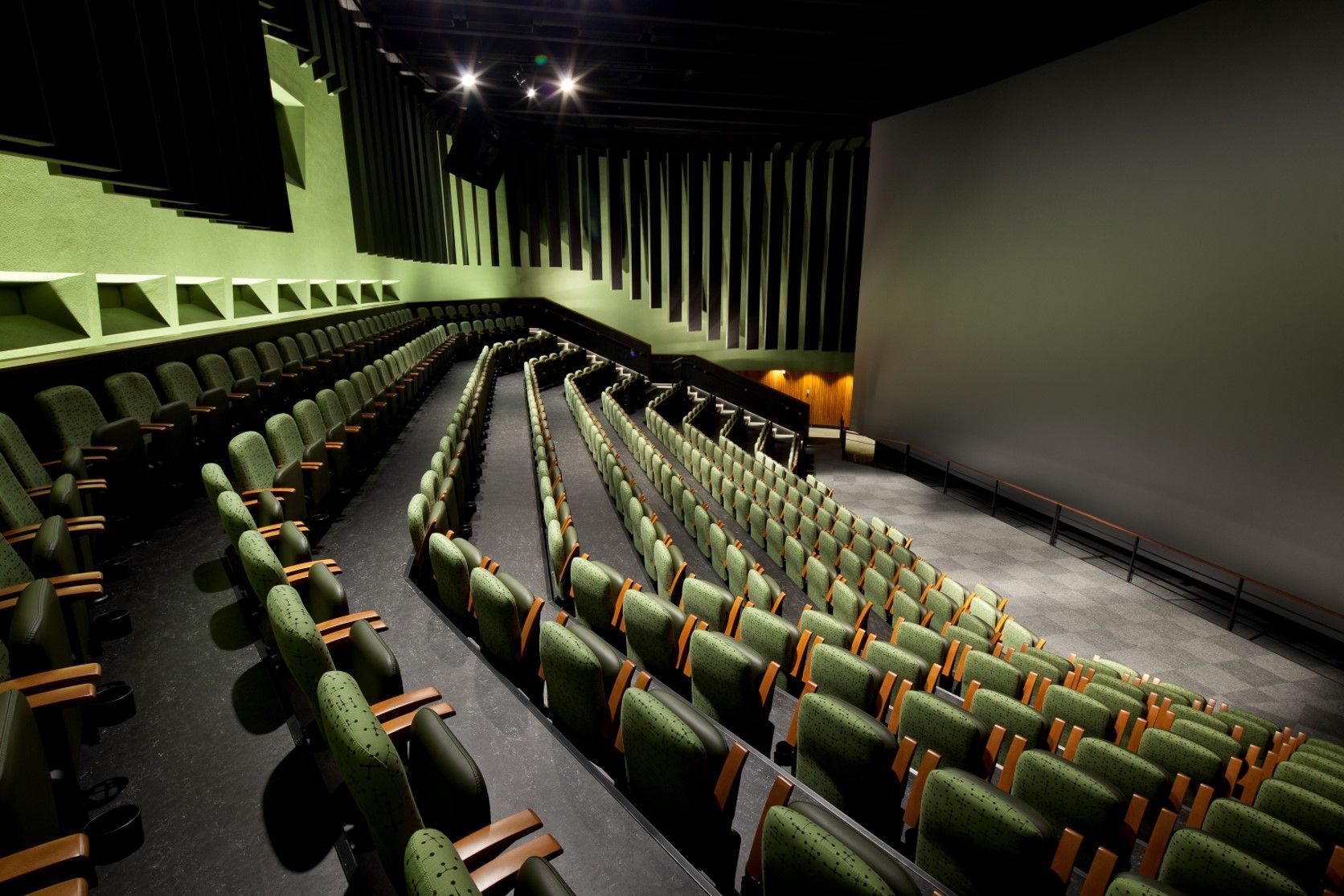Empty movie theater auditorium with green seating and acoustic paneling.
