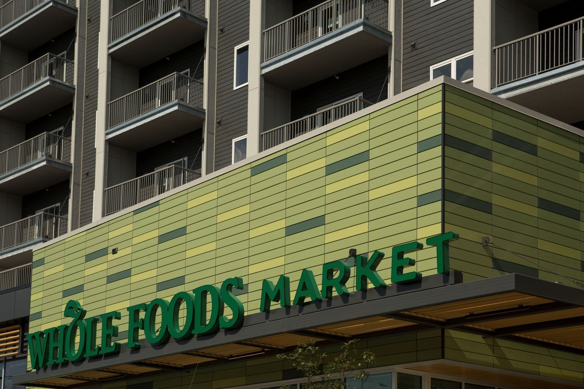 Whole Foods Market storefront, green sign, yellow-green tiled facade, multi-story building with balconies.