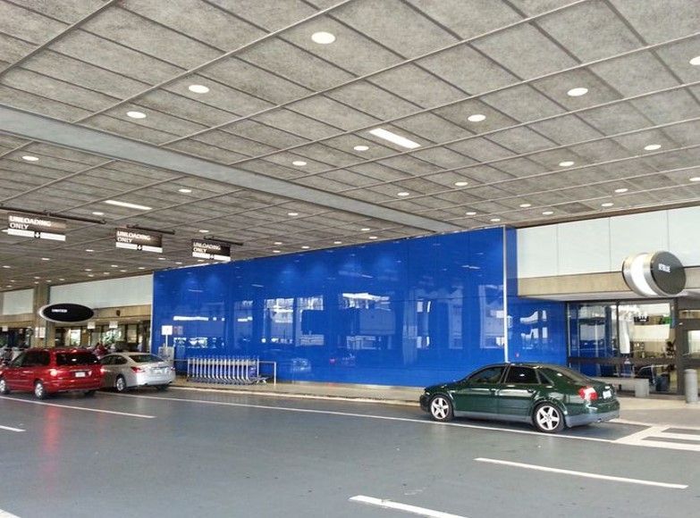 Exterior of a building with blue facade, cars parked in front. Gray pavement and ceiling.