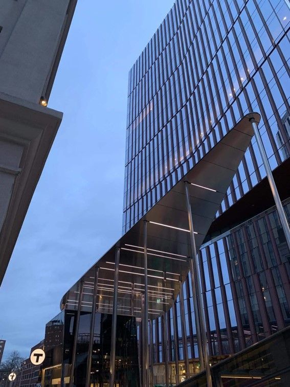 Modern glass skyscraper and metal canopy over a transit entrance at dusk.