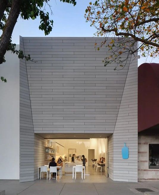 Blue Bottle Coffee shop with a gray facade, open doorway, and customers inside.
