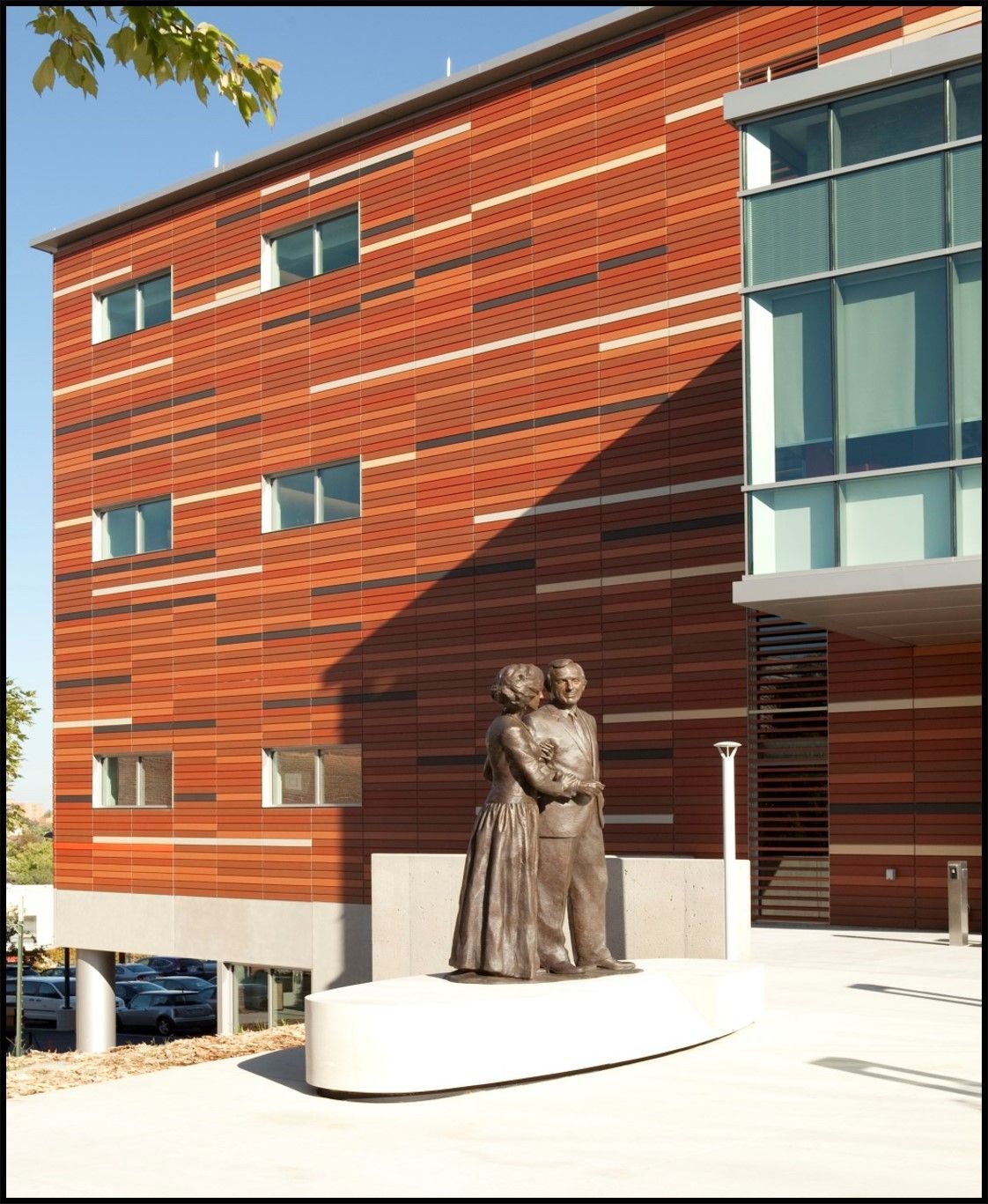 Statue of a couple in front of a red brick building with windows. Building has a glass section.
