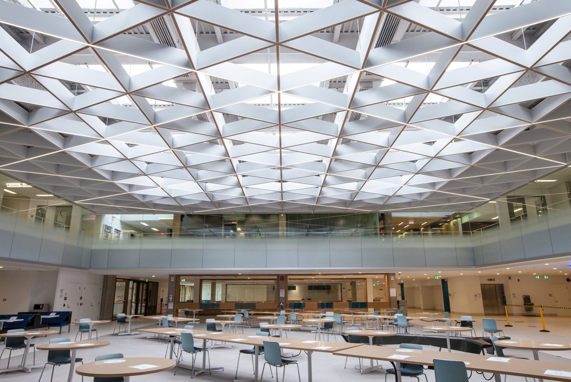 Open interior with a geometric patterned ceiling and tables and chairs on the ground floor.