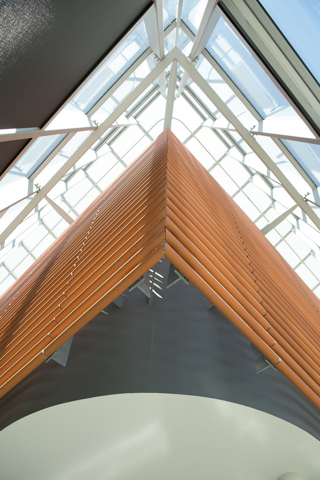 Triangular wooden architectural feature beneath a glass skylight with white beams.