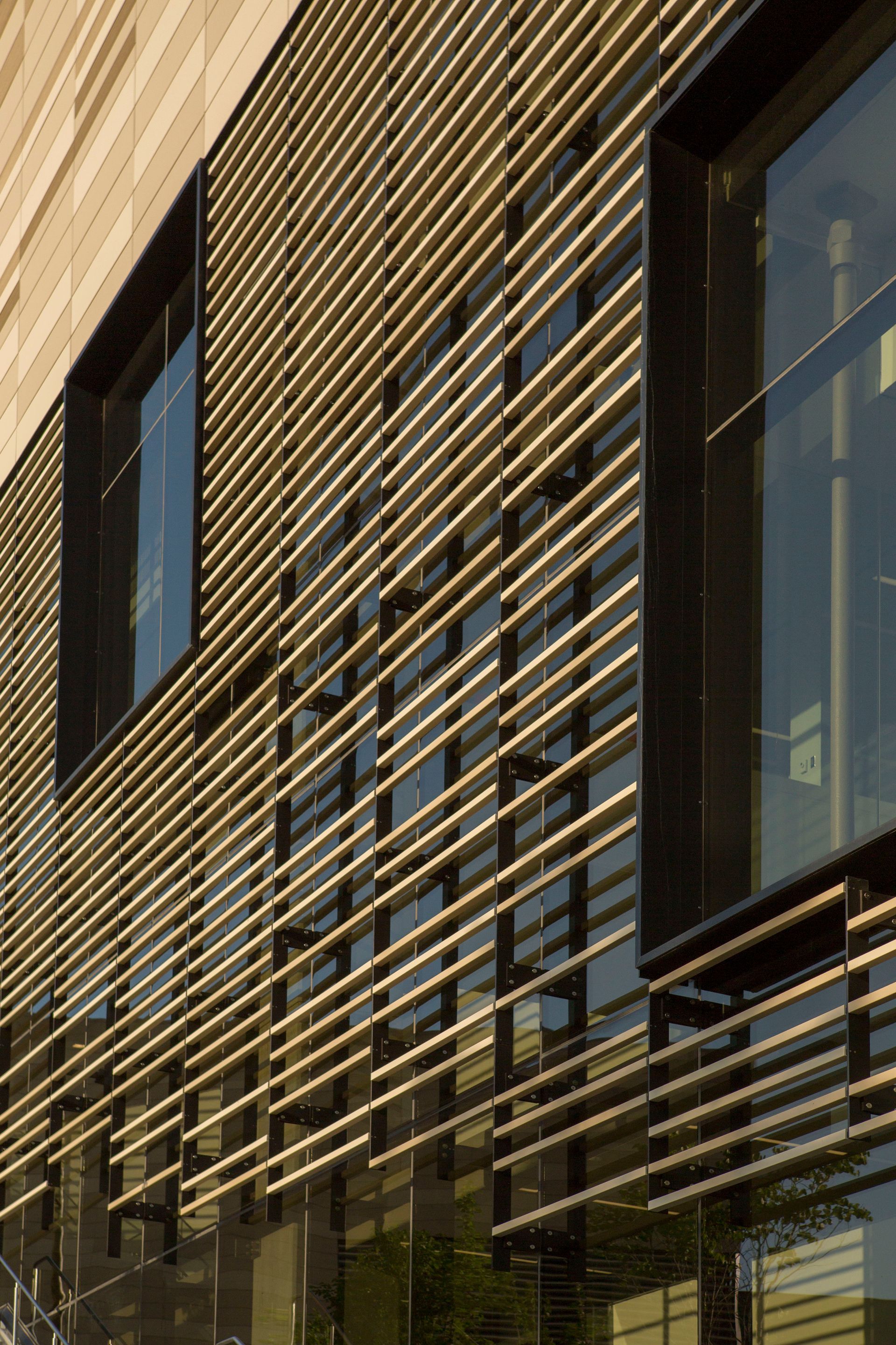 Building exterior with horizontal gold-colored slats over glass windows and a stone wall.