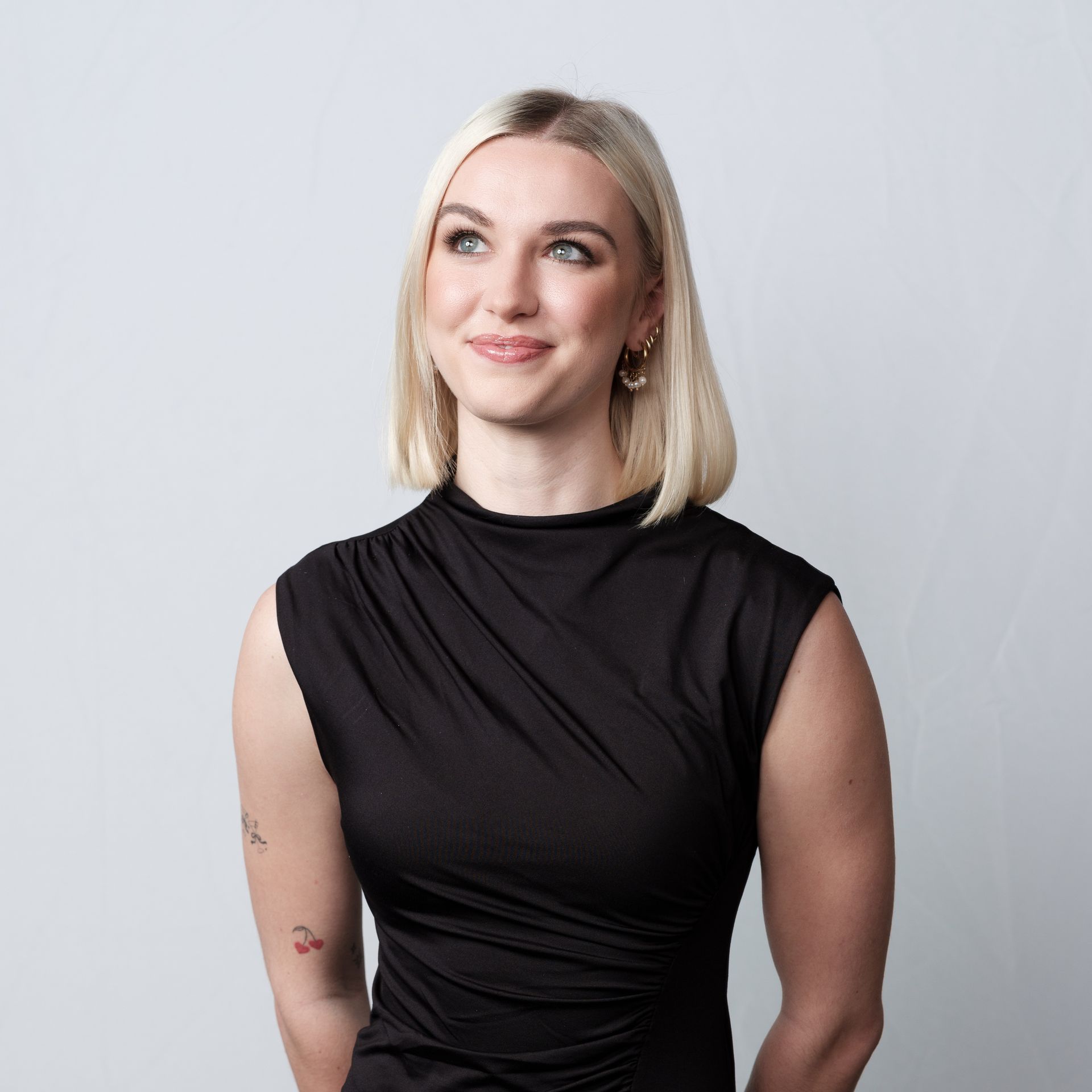 Woman with blonde hair wearing a black sleeveless top, looking upward, smiling slightly. White background.