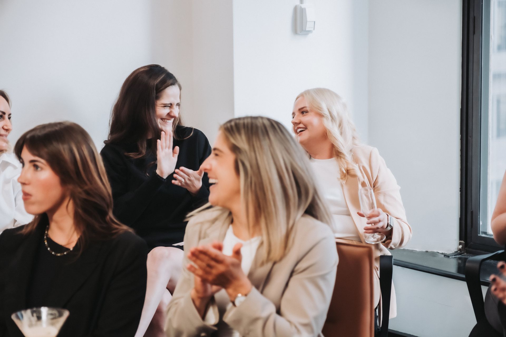 Women applauding in a bright, modern room. Several smiling, with light skin and blonde and brown hair.