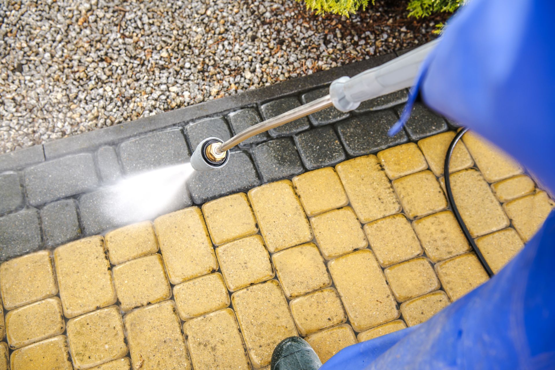 Person pressure-washing a yellow brick walkway and gray curb with a spray nozzle