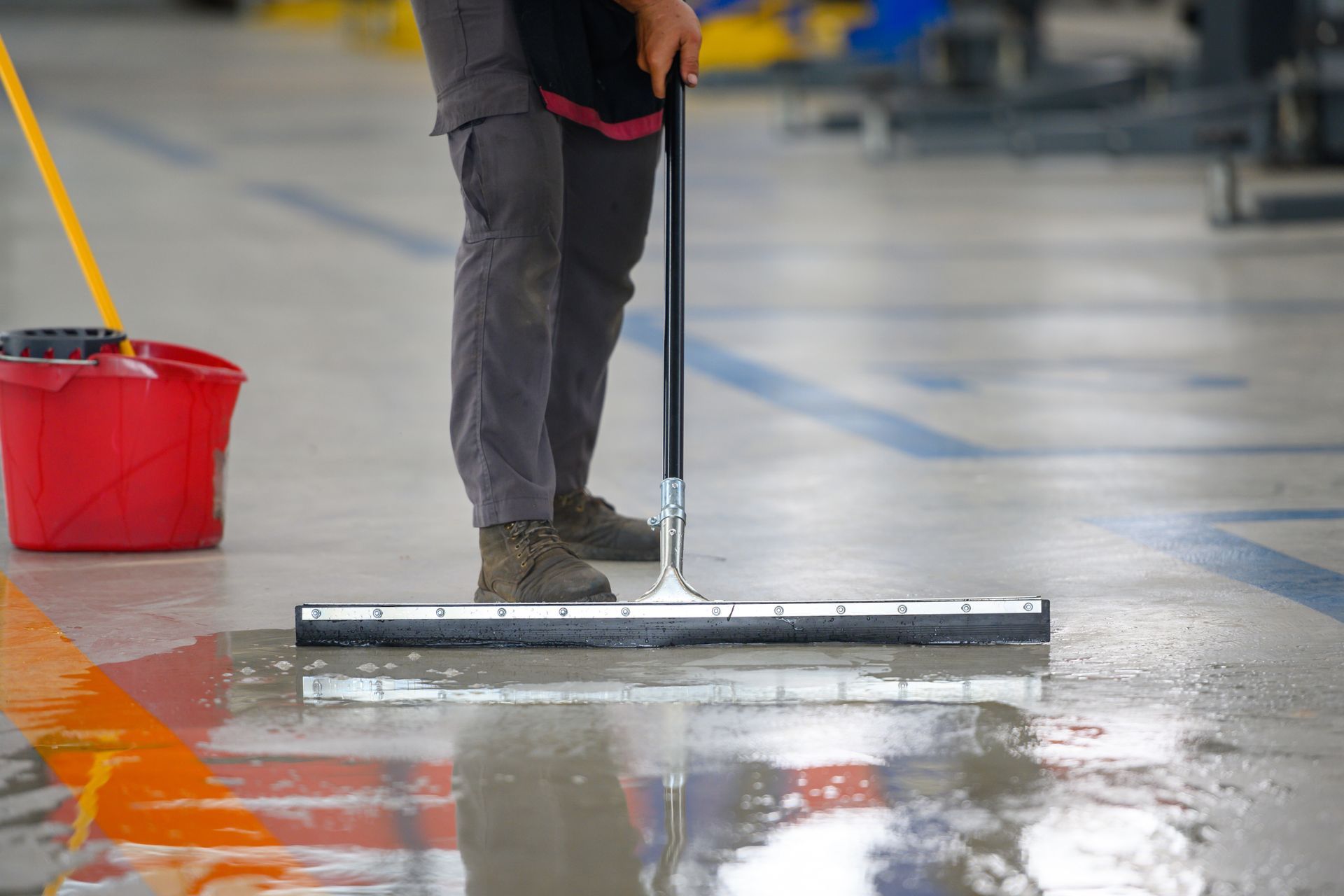 Person mopping a wet floor with a red bucket in a parking garage