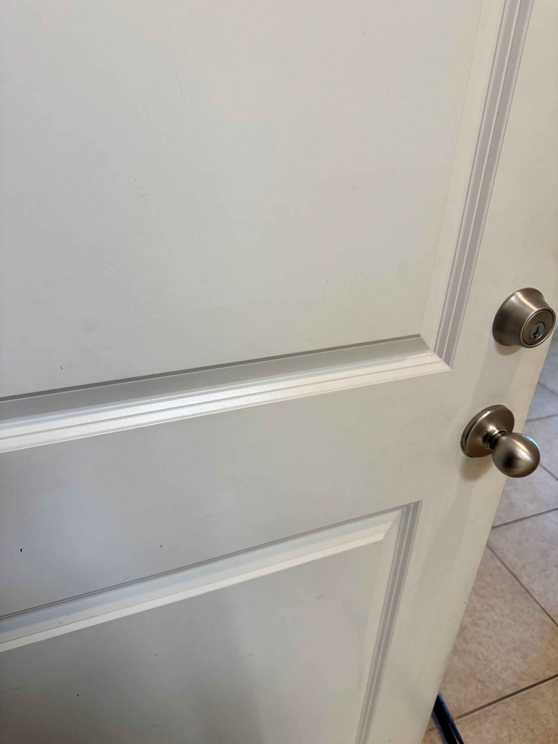 White paneled door with a silver knob, slightly open to a tiled floor.