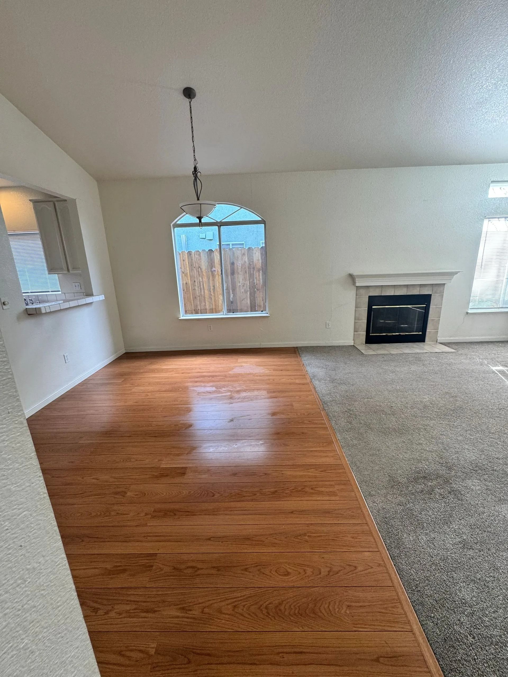 Empty living room with wood and carpet flooring, fireplace, and arched window.