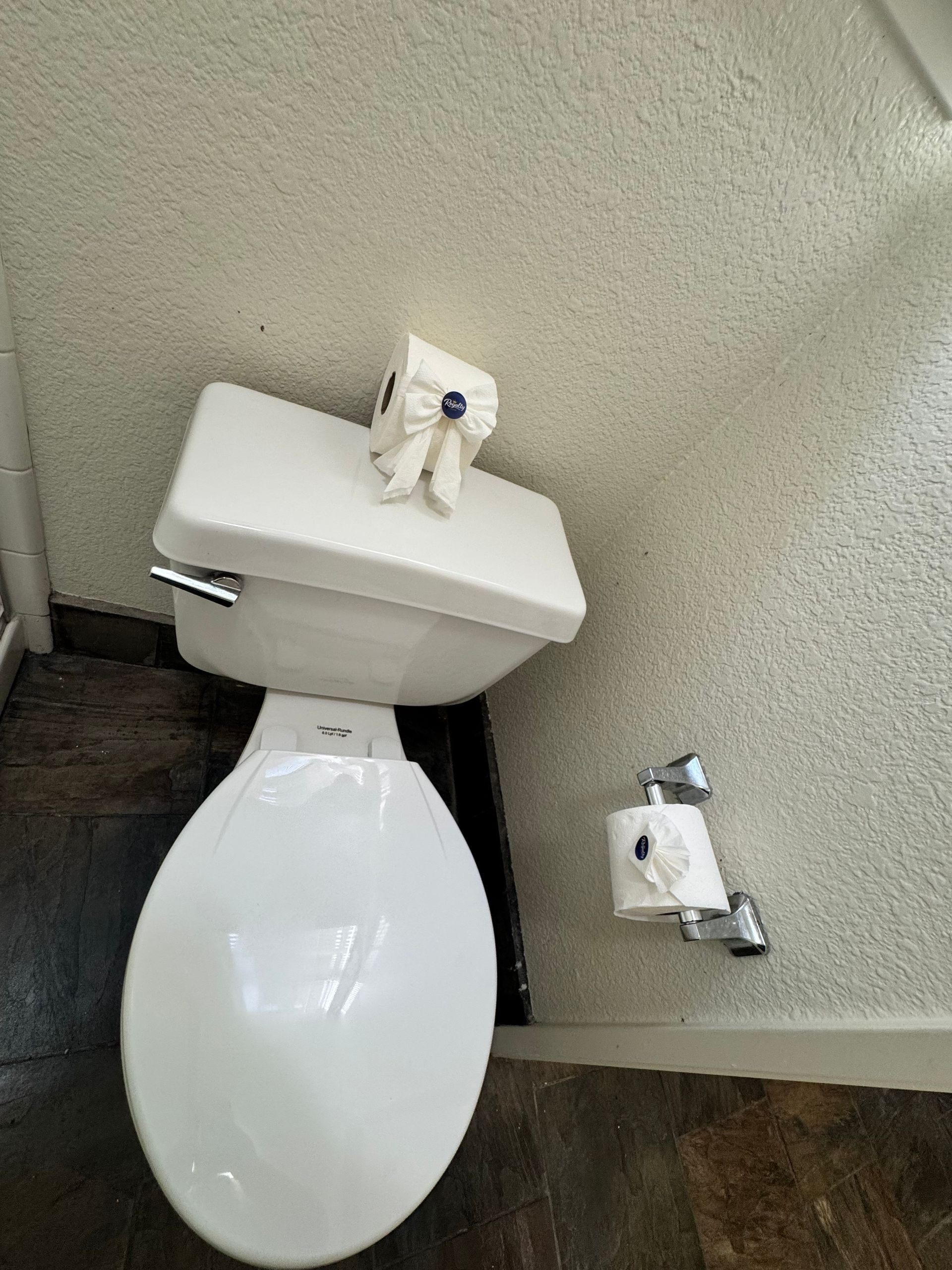 Toilet with a roll of toilet paper on the tank and another on the wall holder in a small restroom.