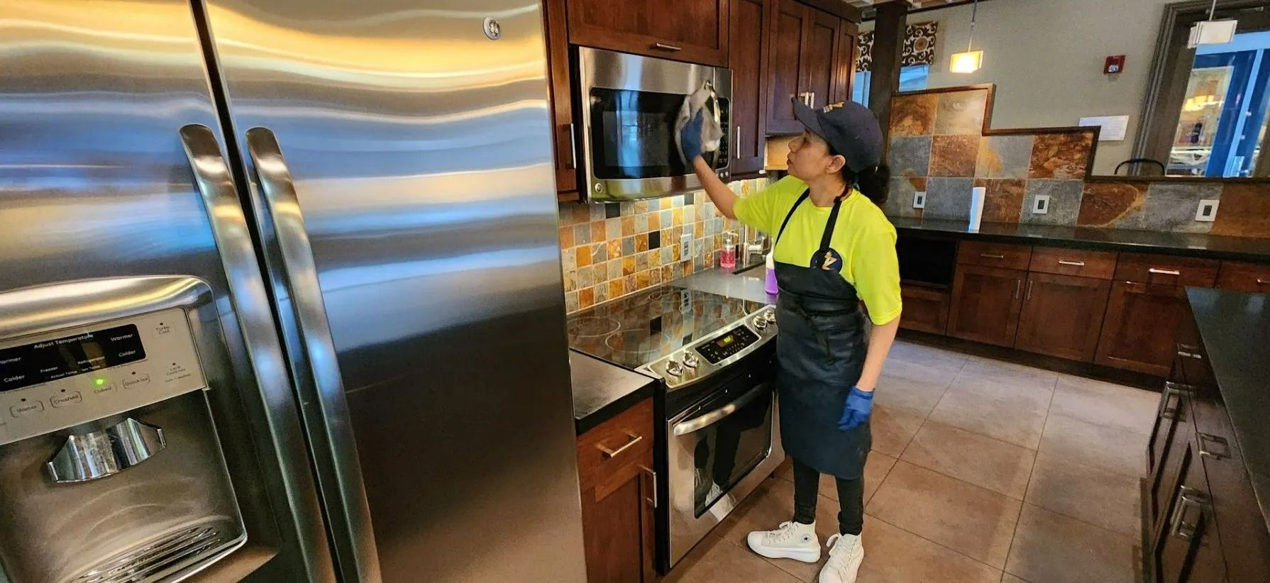 Person in a bright green shirt and apron standing in a modern kitchen, reaching toward the counter.