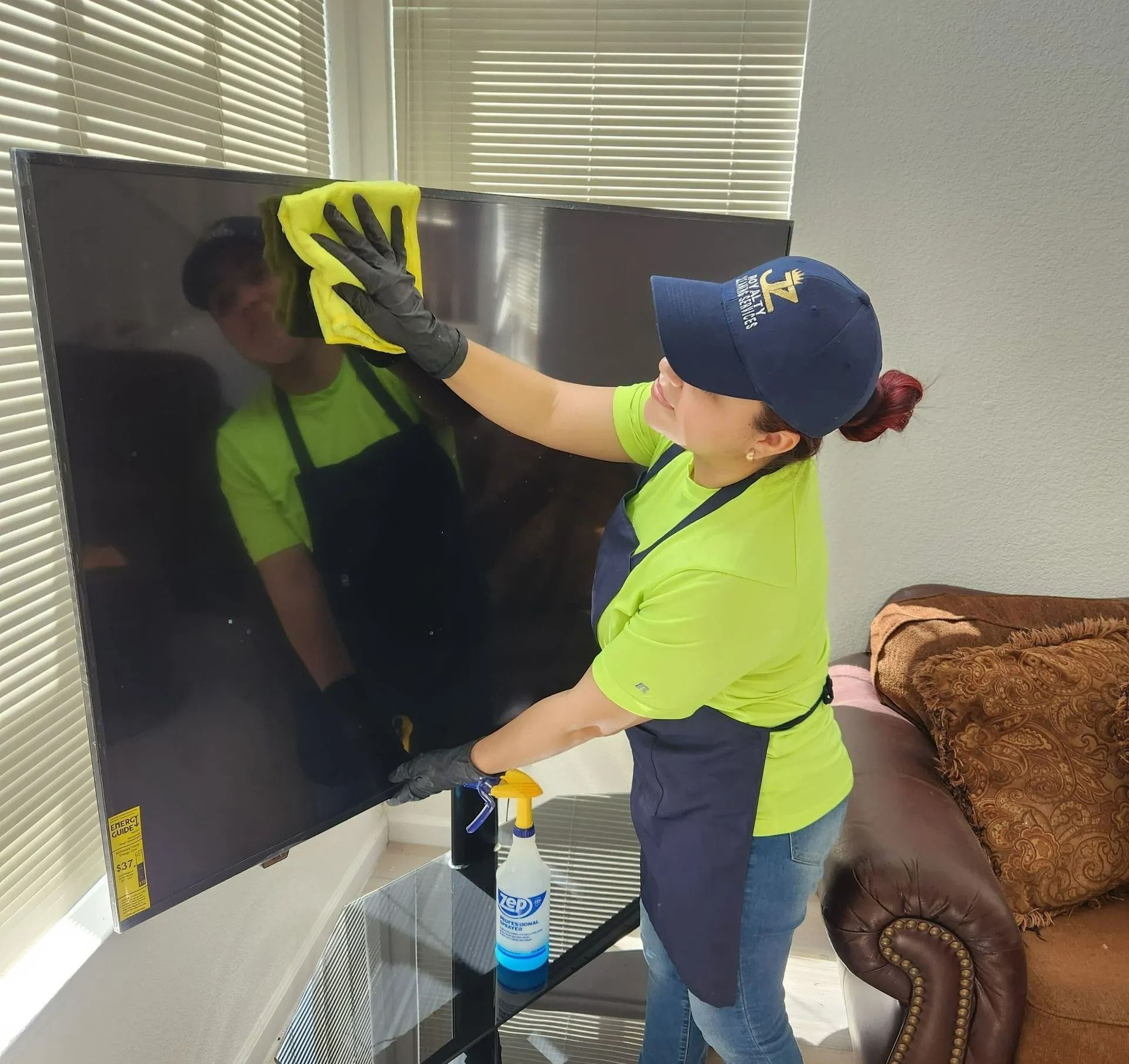 Person cleaning a black TV screen with a spray bottle and yellow cloth in a sunlit room