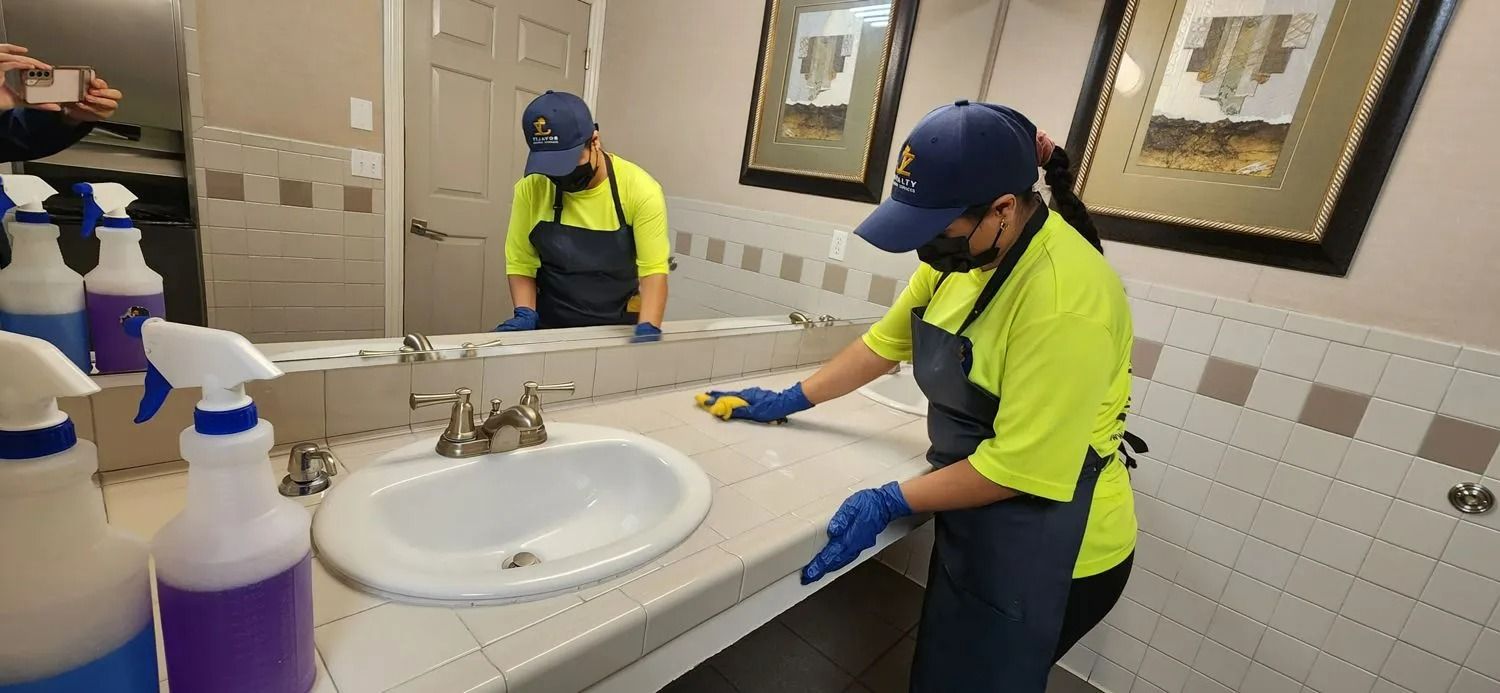 Custodial workers cleaning a tiled bathroom sink counter with spray bottles and blue gloves