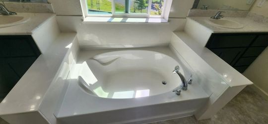 White corner bathtub with built-in steps beneath a window in a modern bathroom