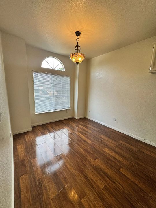 Empty room with glossy wood floors, cream walls, and a hanging pendant light by an arched window.
