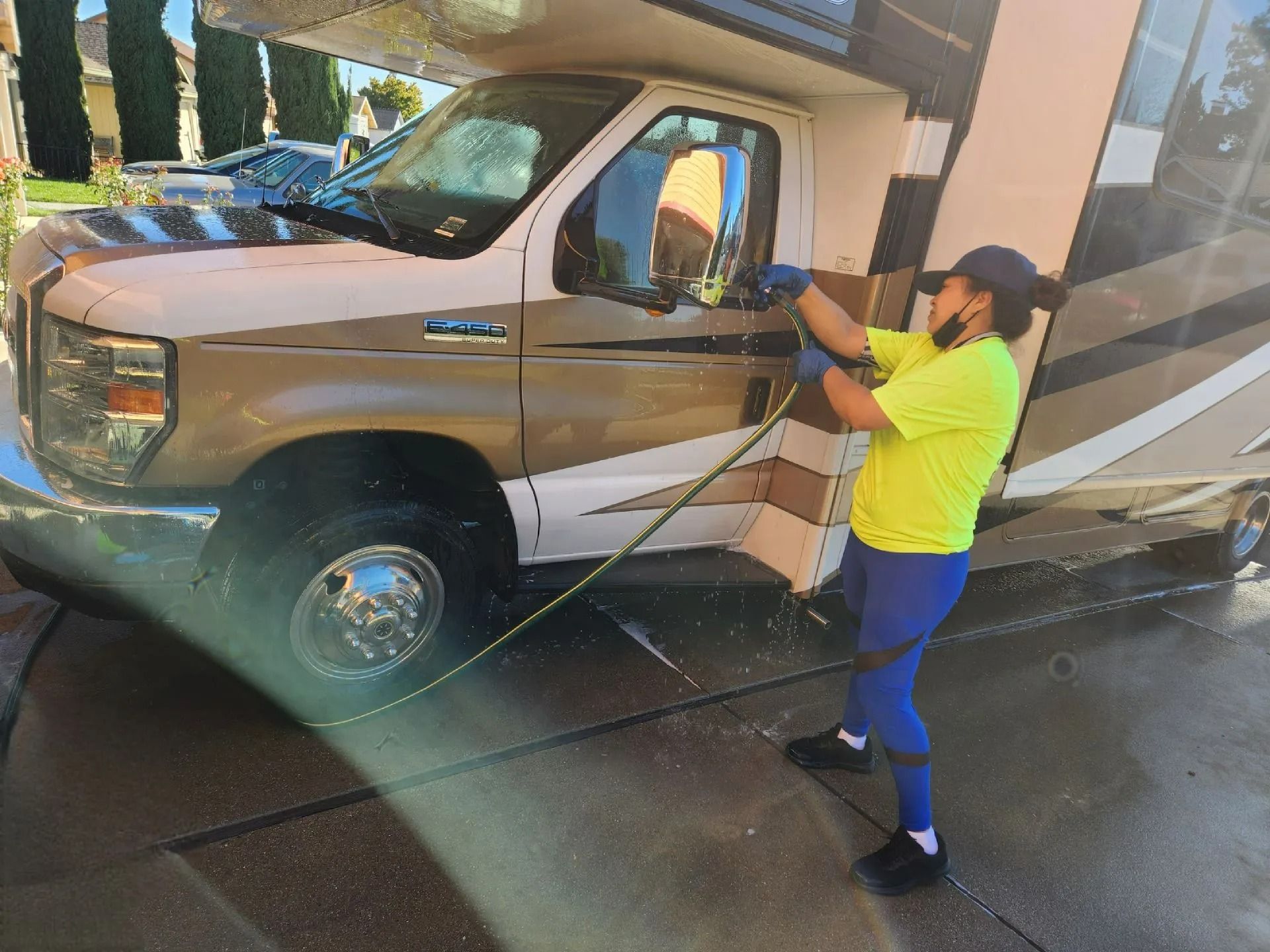 Woman washing tan pickup truck with a pressure washer in a driveway or carport