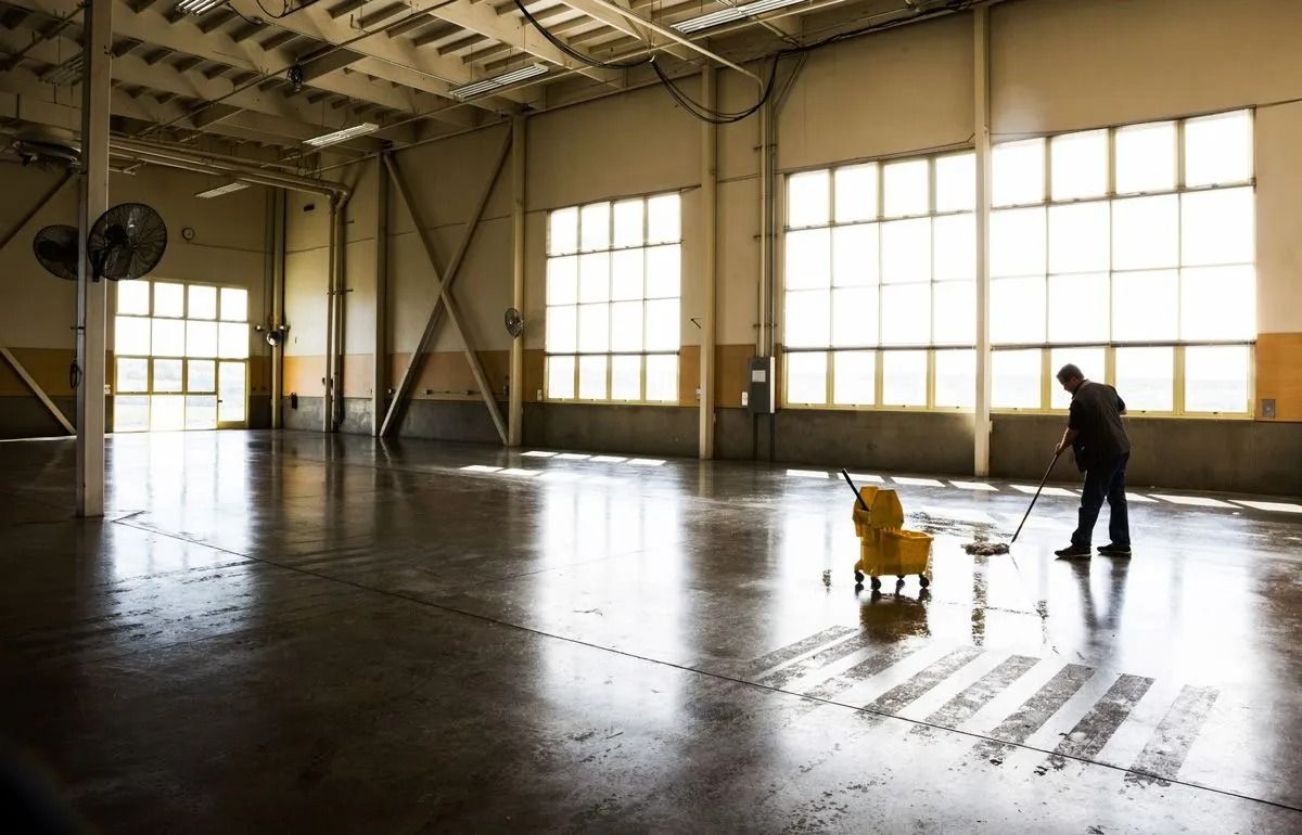 Person mopping a wet warehouse floor in a sunlit industrial space