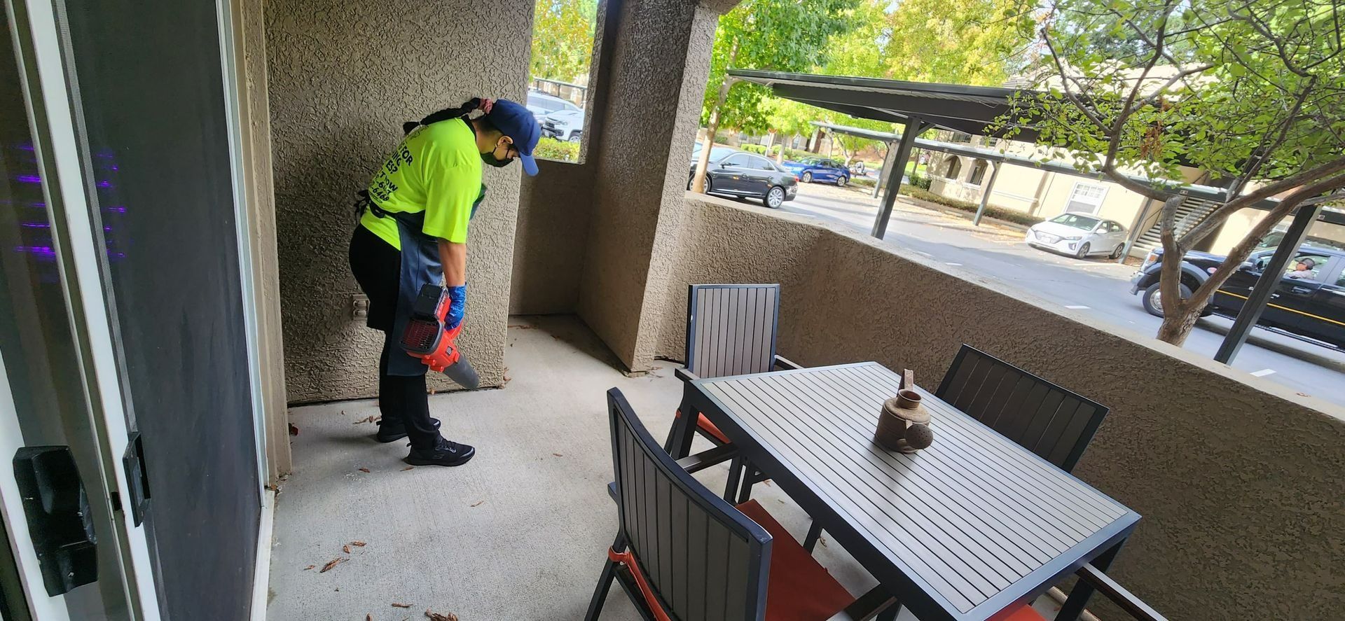 Worker using a leaf blower on an apartment balcony near a table and chairs
