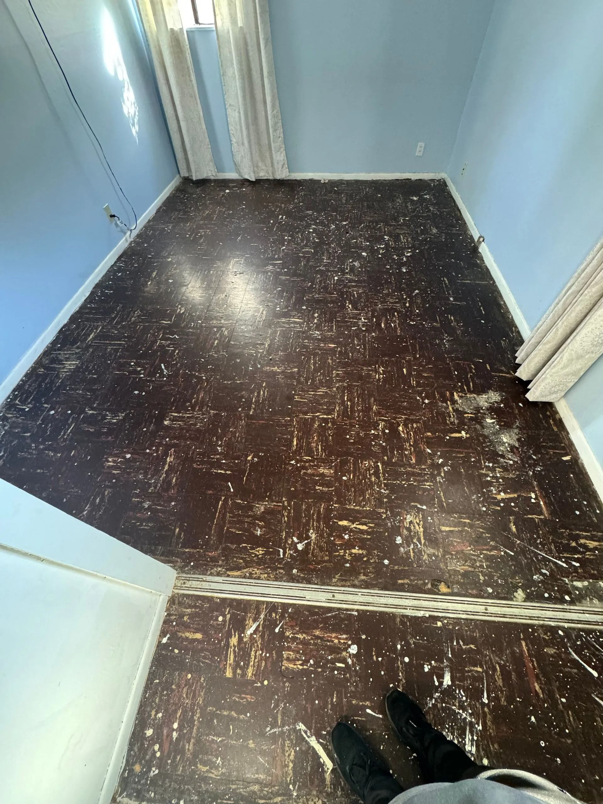 Inside a small blue elevator with a dark speckled floor and a person’s shoes visible at the bottom