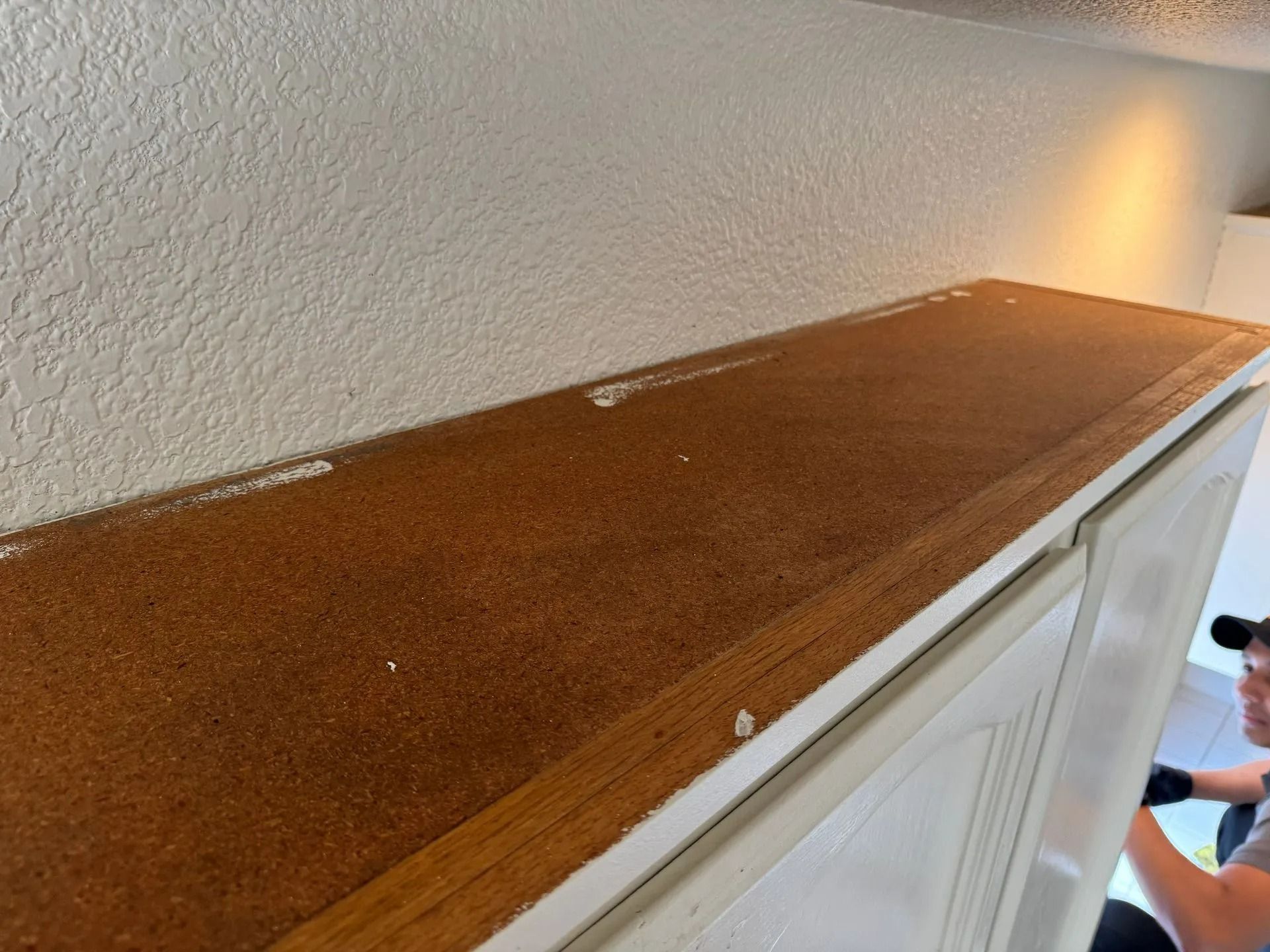 Brown carpeted cabinet top in a hallway, with a person partially visible at the right edge.