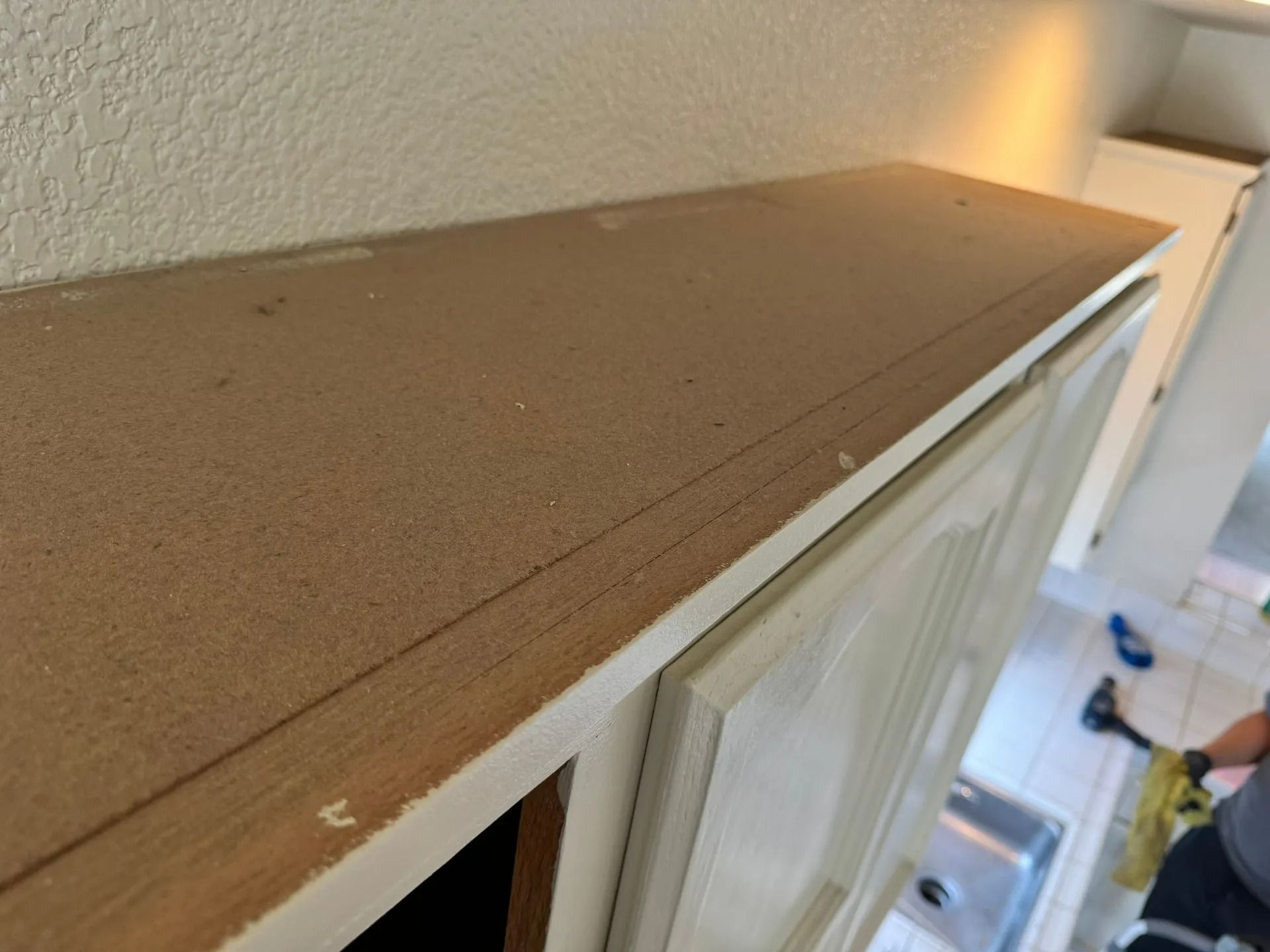 Brown laminate tabletop edge beside a white cabinet or appliance in a home interior