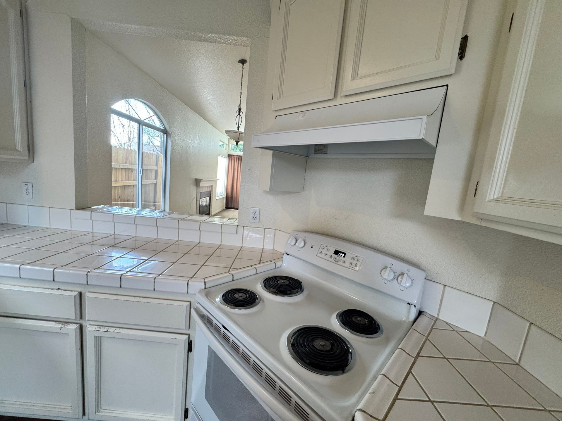 White kitchen with tiled counters, white cabinets, and a black electric stove under a range hood.