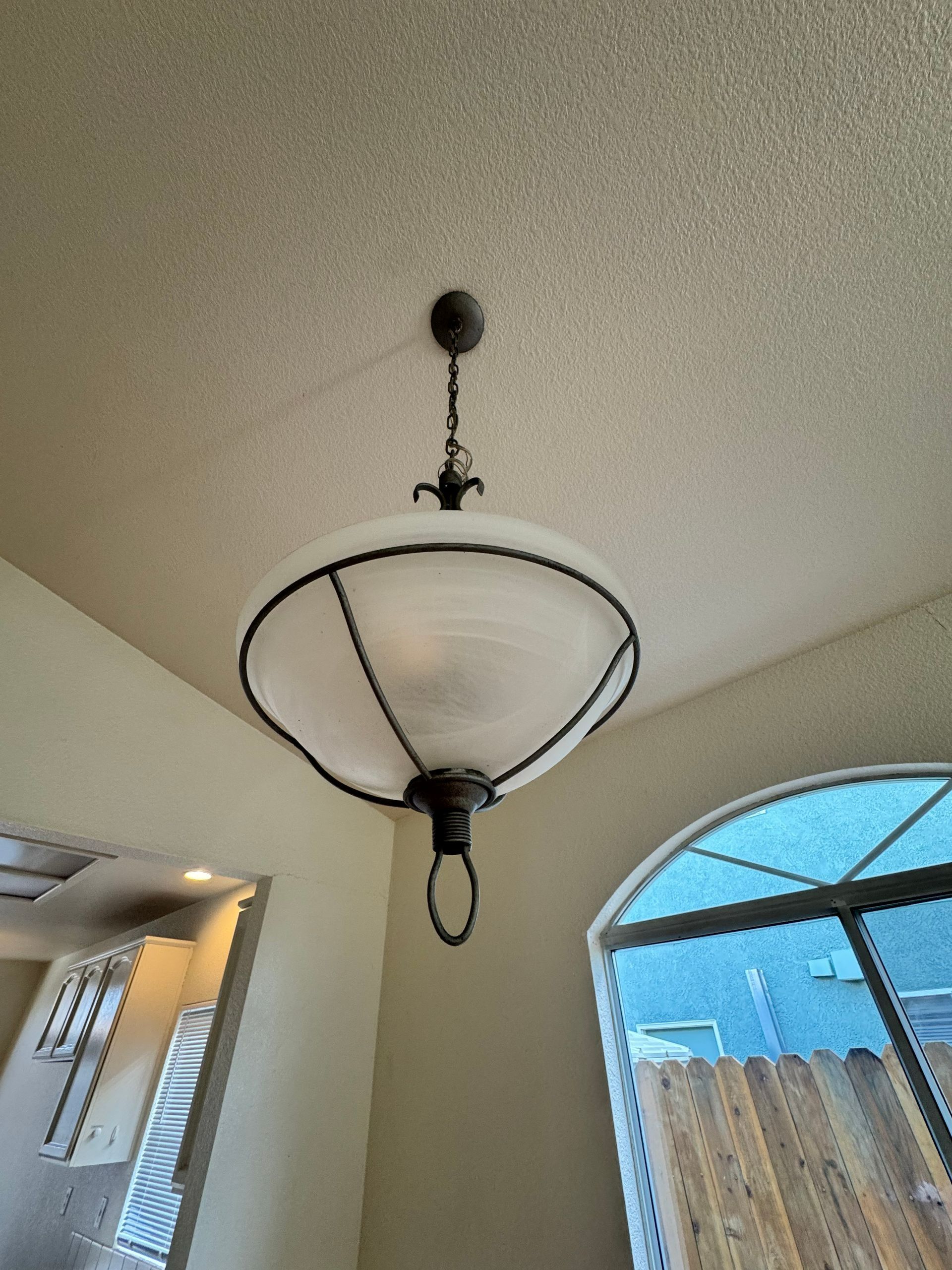 Ceiling light fixture with frosted glass shade in a beige room near an arched window