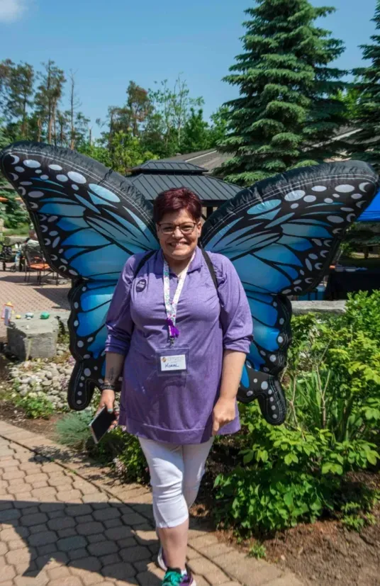 Woman posing in front of a large blue butterfly display in a garden path.