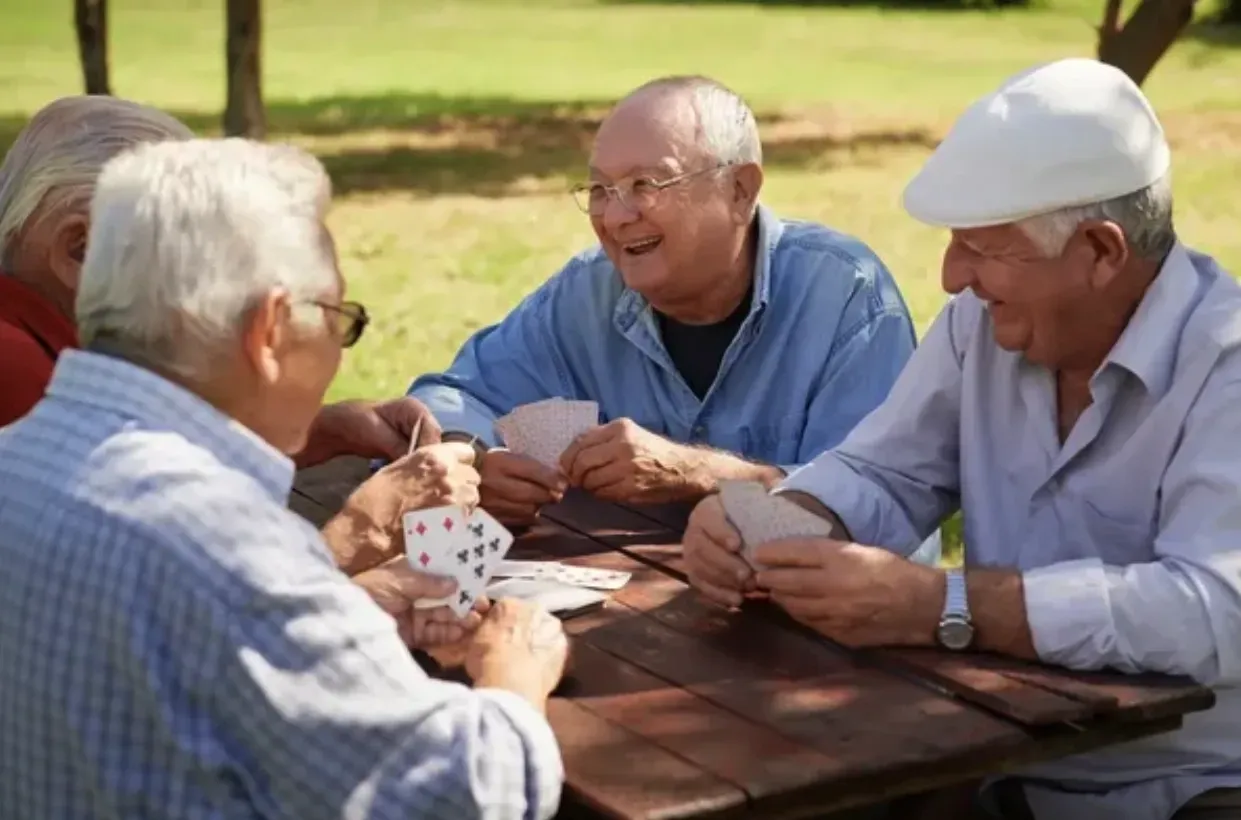 Four people playing cards at a picnic table in a sunny park
