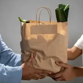 Hands exchanging a brown paper grocery bag with green vegetables visible inside
