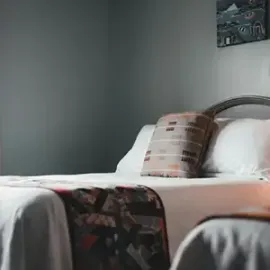 Neatly made bed with white bedding, patterned throw, and plaid pillow in a gray bedroom