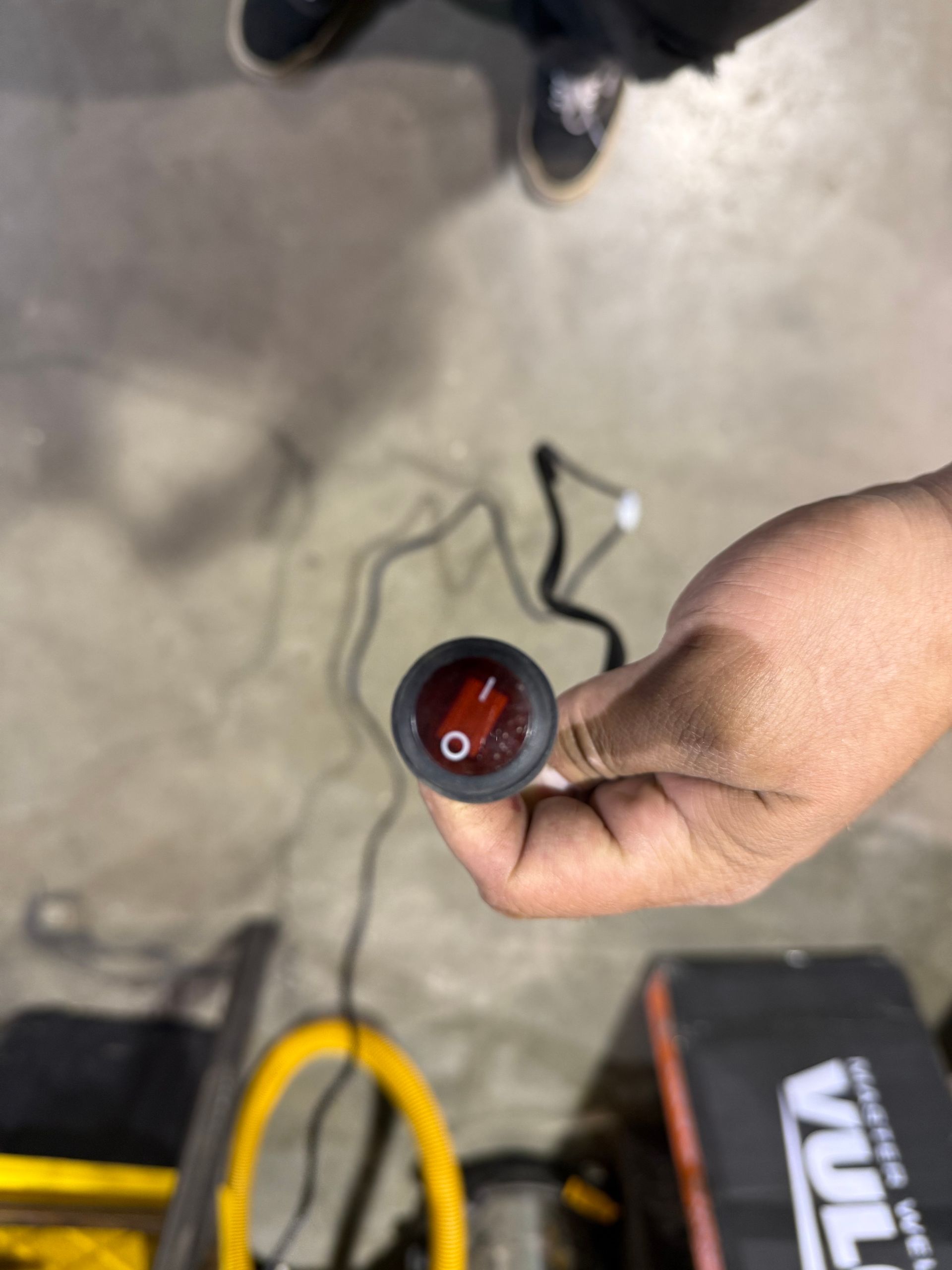 Person holding a small, round, red illuminated switch with black wiring.
