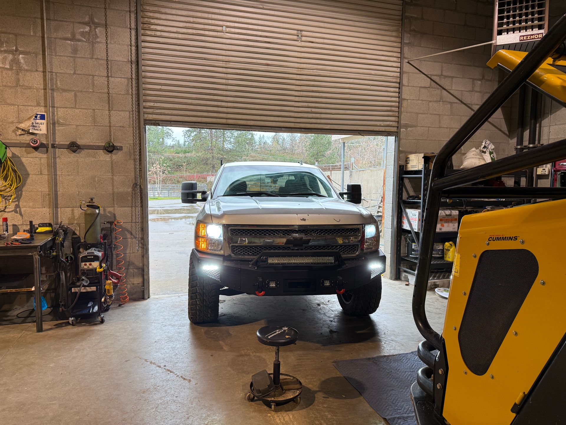 Silver truck in a garage with the garage door open, facing the camera.