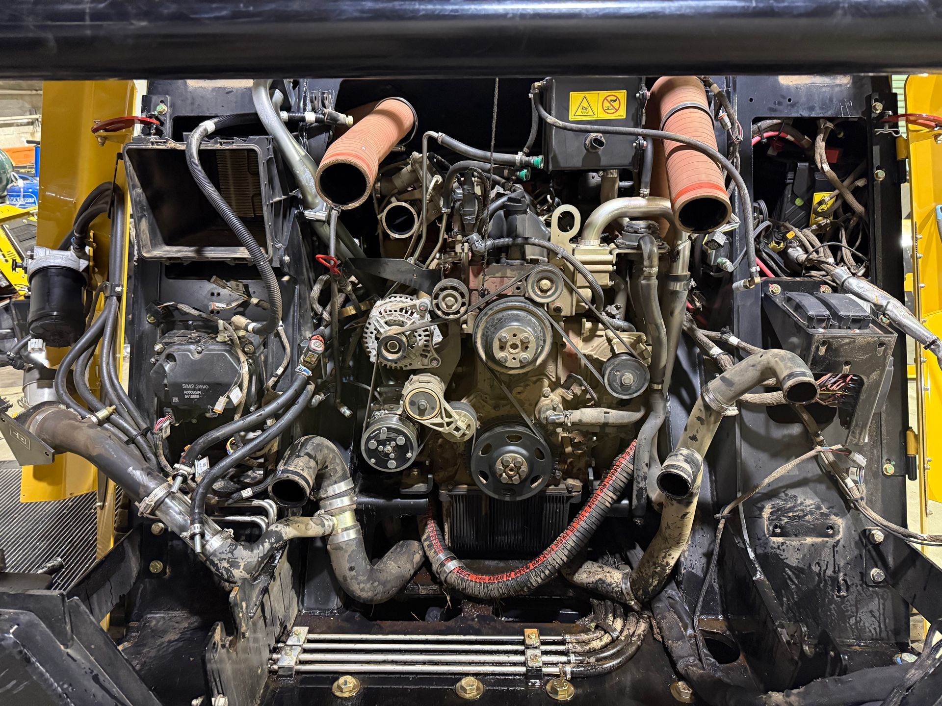An open engine compartment of heavy machinery showing belts, pulleys, and hoses; covered in dirt.