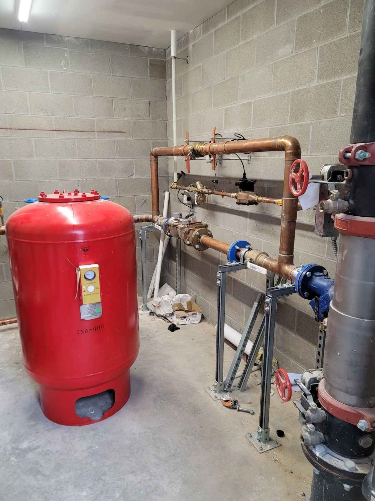 Red pressure tank and copper pipes against cinder block wall.