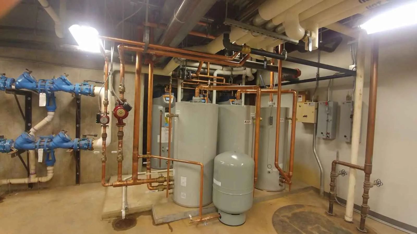 Plumbing equipment: copper pipes, gray tanks, blue valves in a utility room.