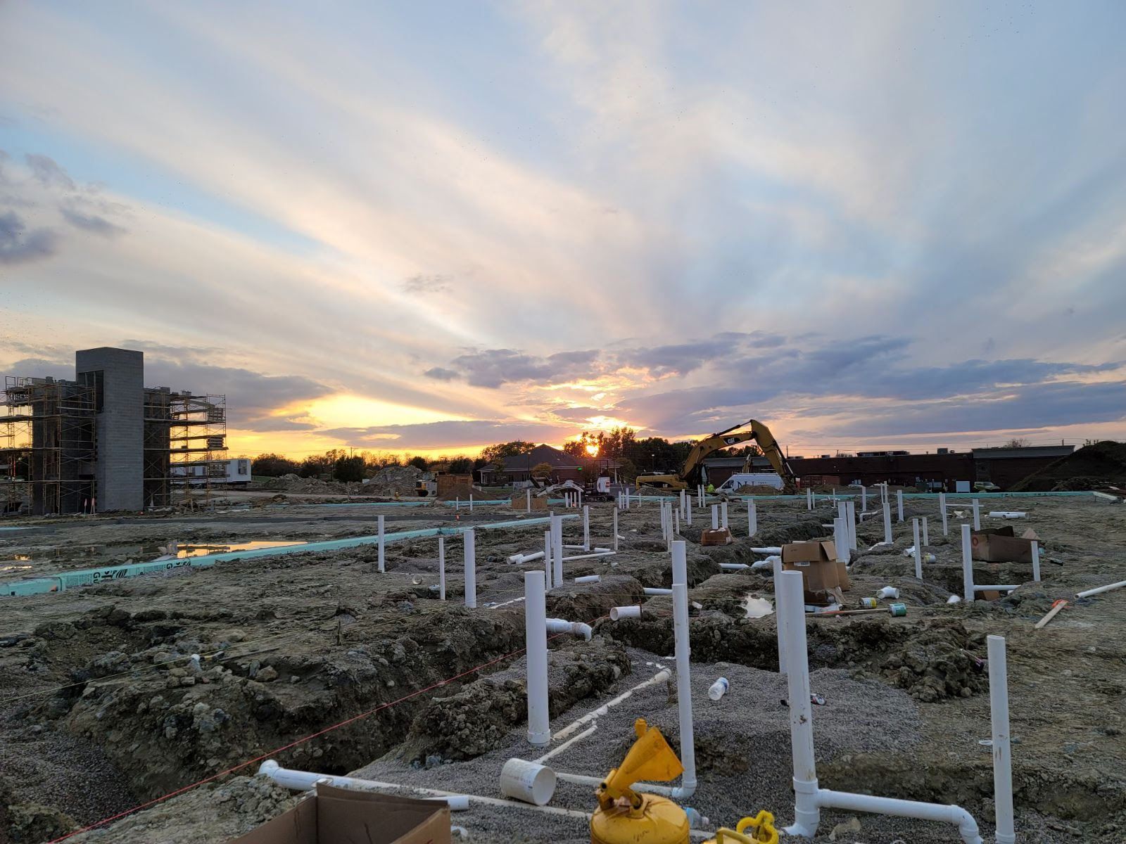 Construction site at sunset with exposed pipes and building skeletons.